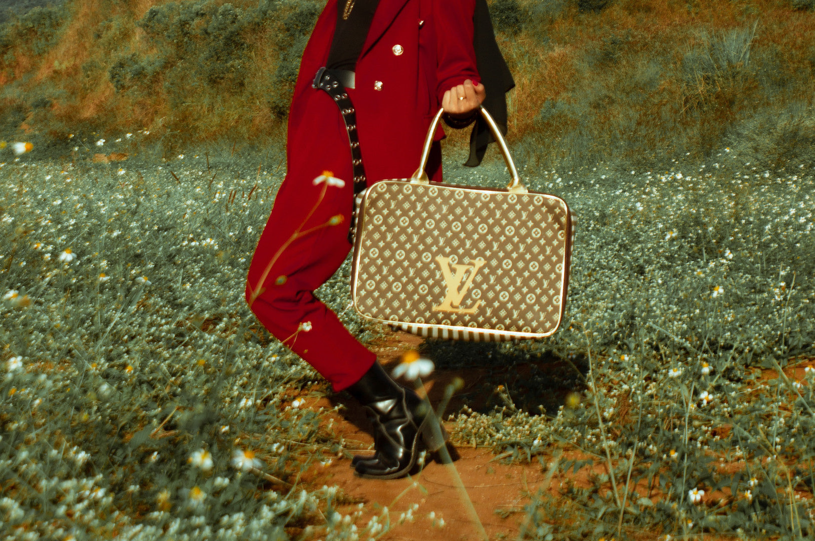 A model walking outdoors displaying a LOUS VUITTON handbag