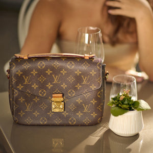 louis vuitton tasche auf einem tisch neben einer kleinen pflanze